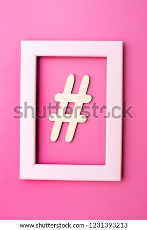 Hashtag sign made of wooden material in frame on pink background. Top view