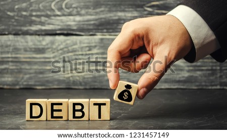 Wooden blocks with the word debt and the image of dollars. Payment of taxes and of debt to the state. Concept of financial crisis and problems. Risk management. Debt exemption. loan Royalty-Free Stock Photo #1231457149