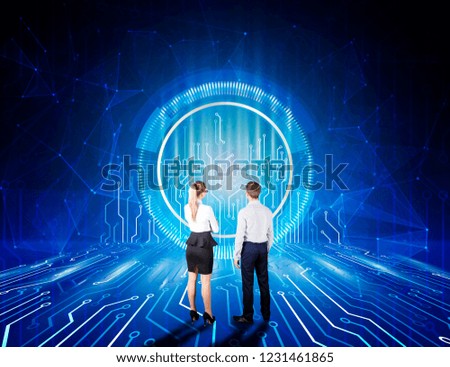 Back view of young businessman and woman looking at information technology processes and big data techno background hologram in futuristic interior. Media concept