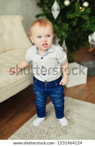 Boy and Christmas. Little blond boy emotional showing grimace in white shirt and blue jeans standing in the room. New year background