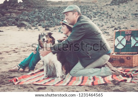 Happy middle age caucasian couple smiling at the beach lovely dog with adult at picnic on the sand -love and frienship enjoying he day outdoor