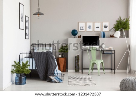 Bright grey bedroom interior with workspace with desk and computer, real photo with copy space on the empty wall