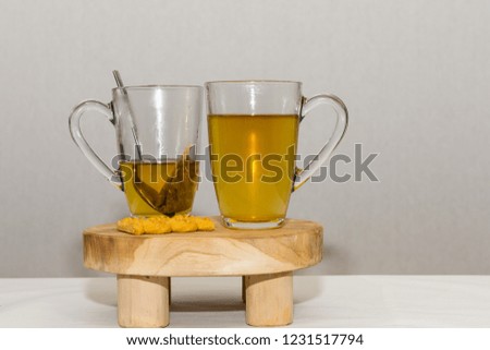 A cookie lays next to two cups of tea.