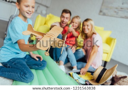 boy playing with toy wooden airplane with family having fun on background and packing for summer holiday
