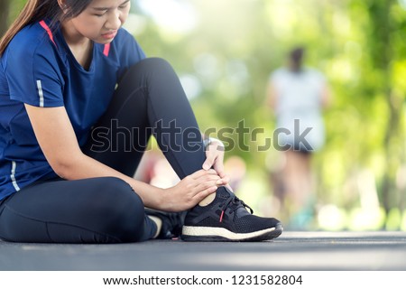 Young asian woman suffering ankle injury. Runner girl is injured by sprain ankle while running or exercising. Female runner touching foot in pain due to sprained ankle. Injury from workout concept Royalty-Free Stock Photo #1231582804