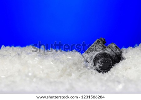 Photo camera frozen in the ice with falling snow on blue background with copy space. Winter background