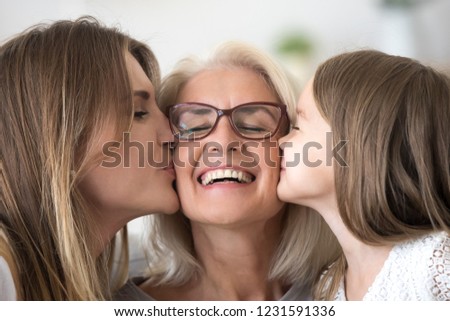 Grown daughter and child granddaughter kissing happy old senior grandmother on cheeks congratulating grandma with mothers day or birthday expressing care and love, three generations of women concept Royalty-Free Stock Photo #1231591336
