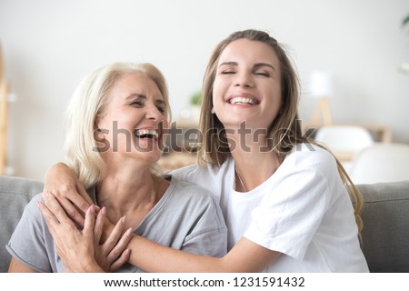 Happy senior mature mother embracing young adult woman laughing together, smiling elderly older mum joking having fun with grown daughter, two age generations humor and positive emotions concept Royalty-Free Stock Photo #1231591432