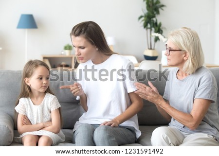 Angry young mother scolding child daughter while old grandmother interfering when strict mom lecturing little girl, three generations disagreements affecting upbringing kid, family conflicts concept Royalty-Free Stock Photo #1231591492