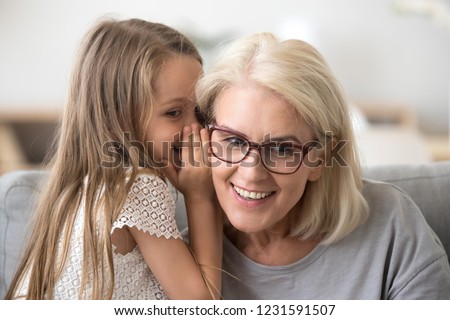 Cute little granddaughter whispering in ear telling secret to understanding smiling grandma, kid girl secretly talking to granny having fun gossiping, trust in grandmother and grandchild relations Royalty-Free Stock Photo #1231591507