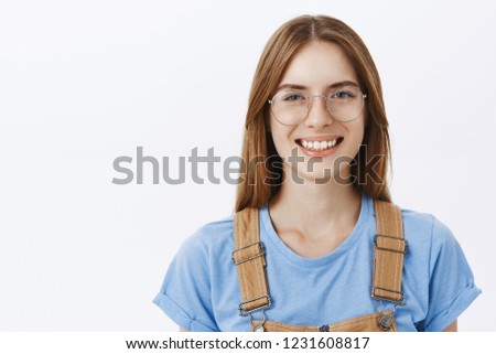 Close-up shot of delighted happy and carefree calm adult female with brown hair in glasses and blue t-shirt smiling friendly at camera having interesting and amusing talk feeling satisfied and joyful