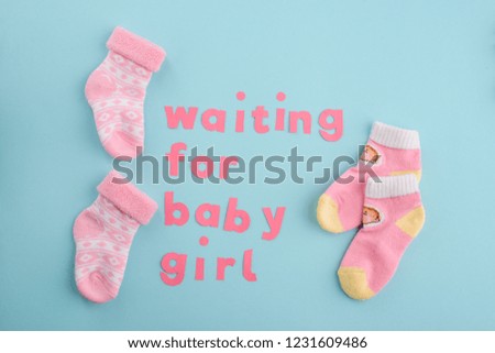 Waiting for a child. Pair of pink socks and paper letters on blue background. Happy news about pregnancy.