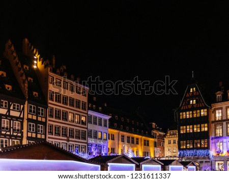 Postcard view with Christmas Market in Strasbourg, France at dusk with illuminated Market Stall chalets in the background and Maison Kammerzell