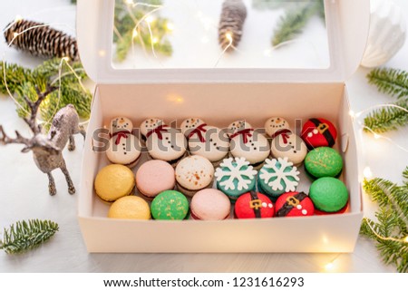 Variety of sweet macaroons in white box. The branches of spruce on bokeh background. Modern european French cuisine. Christmas theme, Merry Christmas card. New year mood. lights of garland bulbs