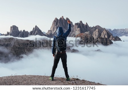Conquest that hill. Touristic man raised his right hand up on the beautiful daylight mountains full of fog. Royalty-Free Stock Photo #1231617745