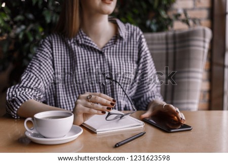  young woman holding eyeglasses while sitting at table with coffee cup in cafe