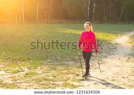 Smiling girl leading active lifestyle engaged in Nordic walking on the track at the setting sun.