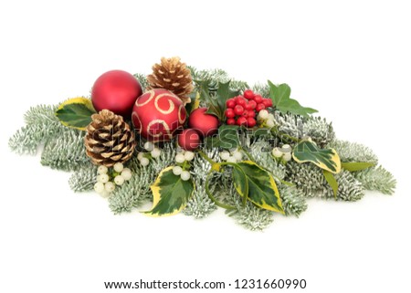 Christmas table decoration with red bauble decorations, holly berries, snow covered spruce pine, ivy, pine cones and mistletoe on white background.