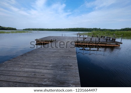 wooden and composite material foot bridge over water in green summer forest surroundings with lake