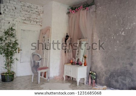 Lateral view of a vintage room in a photo studio with a white vintage wooden dressing table with a big mirror, vases with flowers, a black mannequin with a dress from pink curtain 