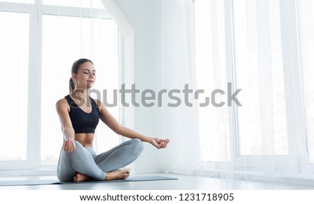 Keep calm. Attractive young woman sitting on lotus position on floor with eyes closed, practicing yoga at home, copy space