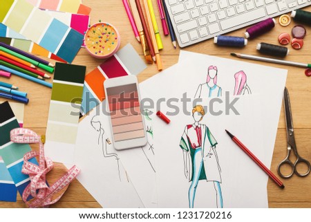 Creating new fashion collection background. Hand drawn sketches of clothes, smartphone with color swatches on screen and threads on wooden table, top view. Creativity, dressmaking and design concept