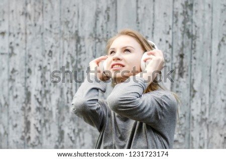 Cute girl listening to music in white wireless headphones on the background of the old board. Electronic music. Musical style. Pleasant sounds. The pleasure of sound.