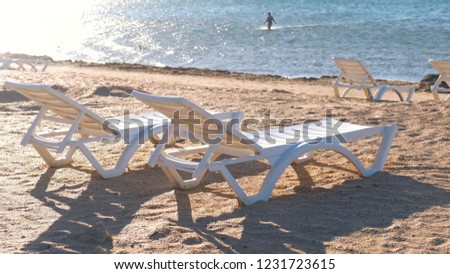 Two plastic white sunlongers on the sand beach near the sea. Royalty-Free Stock Photo #1231723615