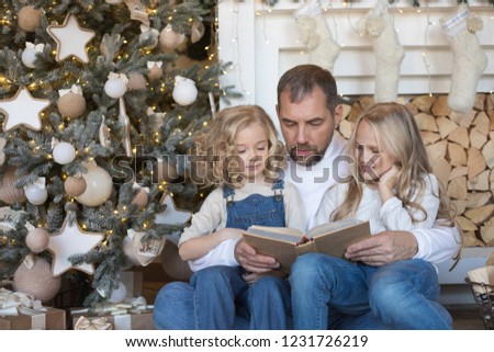 Dad reads daughters a book near the Christmas tree.