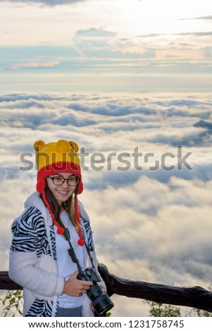 Woman tourist holding a DSLR camera on beautiful nature landscape of fog is like the sea in the winter during sunrise background at high viewpoint Phu Ruea National Park, Loei province, Thailand