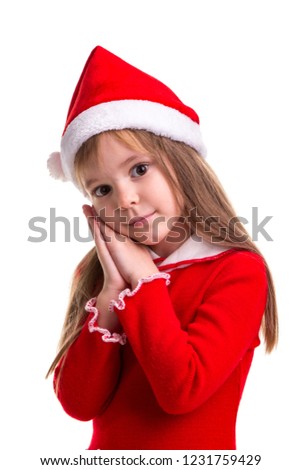 Coquettish christmas girl wearing a santa hat isolated over a white background, holding her hands under the right chin, looking sadly straight. Portrait picture