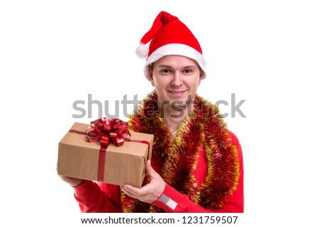 Funny smiling guy with a Santa hat, tinsel around the neck, holding the gift box in the hands