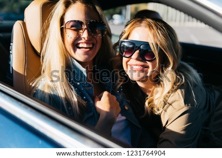 Photo of blondes wearing sunglasses while driving in car
