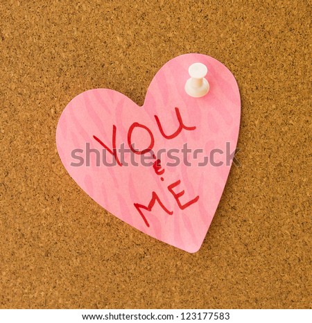 You & Me written on pink heart memo with pattern attached to cork board with white push pin