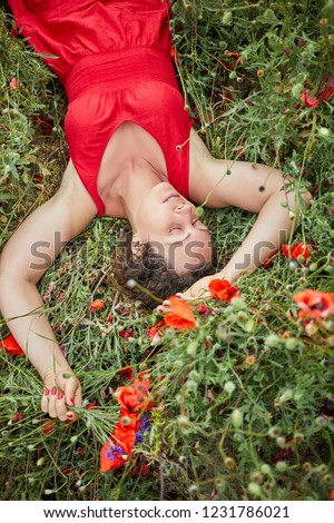 Woman in red dress sleeps lying on red poppies field.