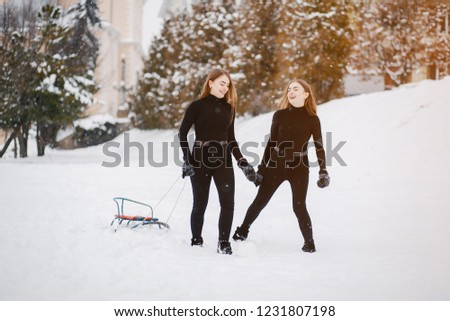 Cute girls in a winter park. Sisters have fun with sled