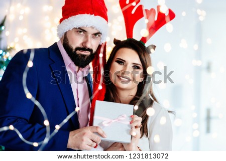 Happy couple in Christmas hats holding gift box. Man and woman at christmas