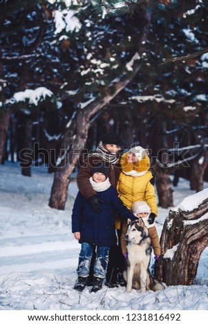 Happy european young family with big dog posing against winter pine forest. The concept of a winter holiday. Photo with background blur. Vertical photo of a family in full growth.