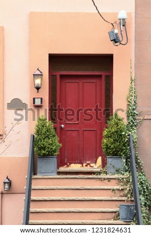Dark red vintage wooden entry door with steel doorknob, gray flower pots and thuja bushes. New Jersey. USA.