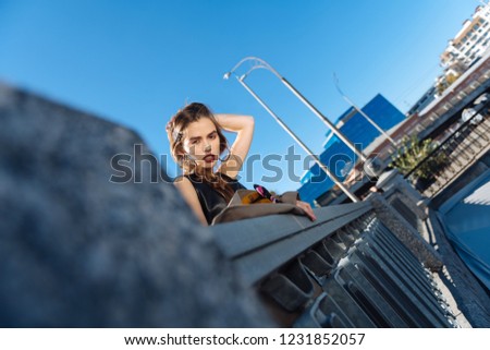 Nice hairstyle. Low angle of beautiful appealing stylish woman with nice hairstyle standing on the bridge