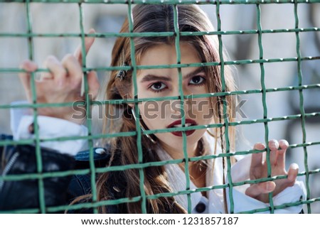 Near fence. Beautiful dark-eyed model with bright lips wearing leather jacket posing near the fence