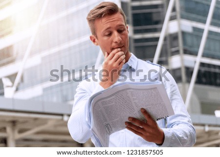 Businessman reading newspaper feeling serious while standing in urban background. Handsome men holding newspaper in his hand with worried about problem something.