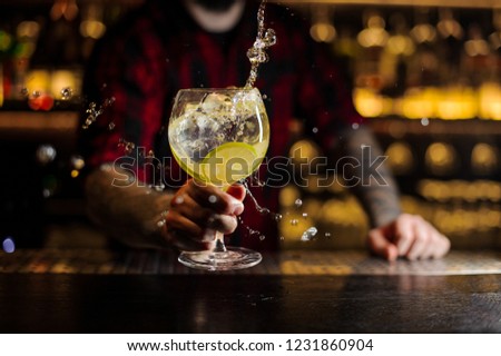 Bartender making splash of a delicious Gin Tonic cocktail with lime slices on the steel bar counter on the blurred background Royalty-Free Stock Photo #1231860904