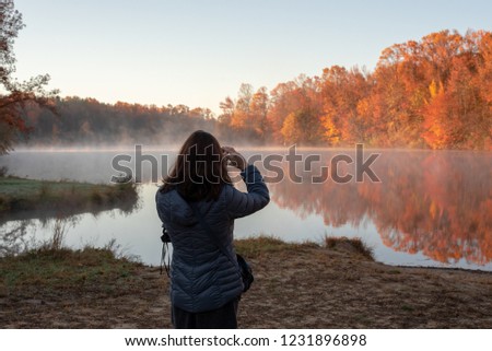 A woman takes pictures of a foggy autumn pond