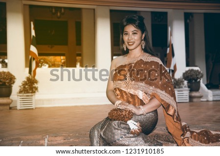The pretty Thai lady in Middle Thai classical traditional dress suit sitting is posing in a Thai temple background. 
