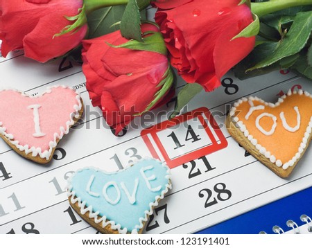 red roses lay on the calendar with the date of February 14 Valentine's day and cookies with the words "I love you"