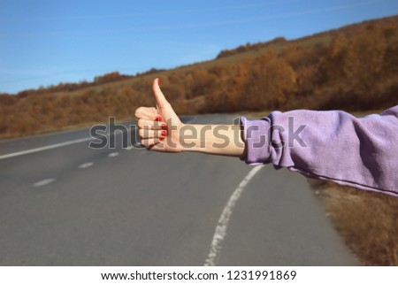 Woman hitchhiking on mountain road, focus on hand