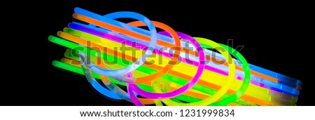 Colorful fluorescent light neon glow stick bracelet strap wristband and tubes on mirror reflection black background. Yellow Blue pink orange green violet glow sticks