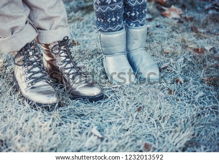 A portrait of a happy family: a young beautiful woman with her little cute daughter walking in the winter city park. Two pairs of legs stand on the snow-covered grass. 