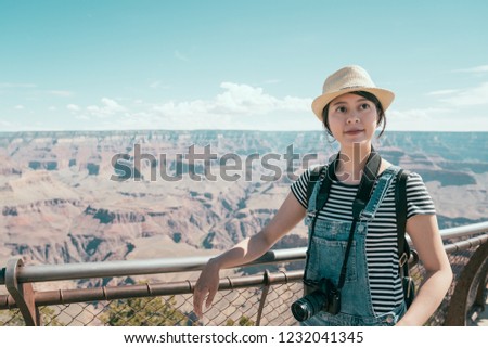 Beautiful girl exploring Grand Canyon national park in Arizona, USA. young asian female traveler with straw hat standing high in the nature dessert. lady tourist carrying camera sightseeing mountain.